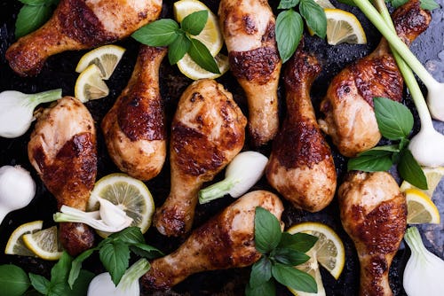 Roasted chicken legs with lemon slices. onion, garlic and basil herbs on rural baking tray viewed fr...