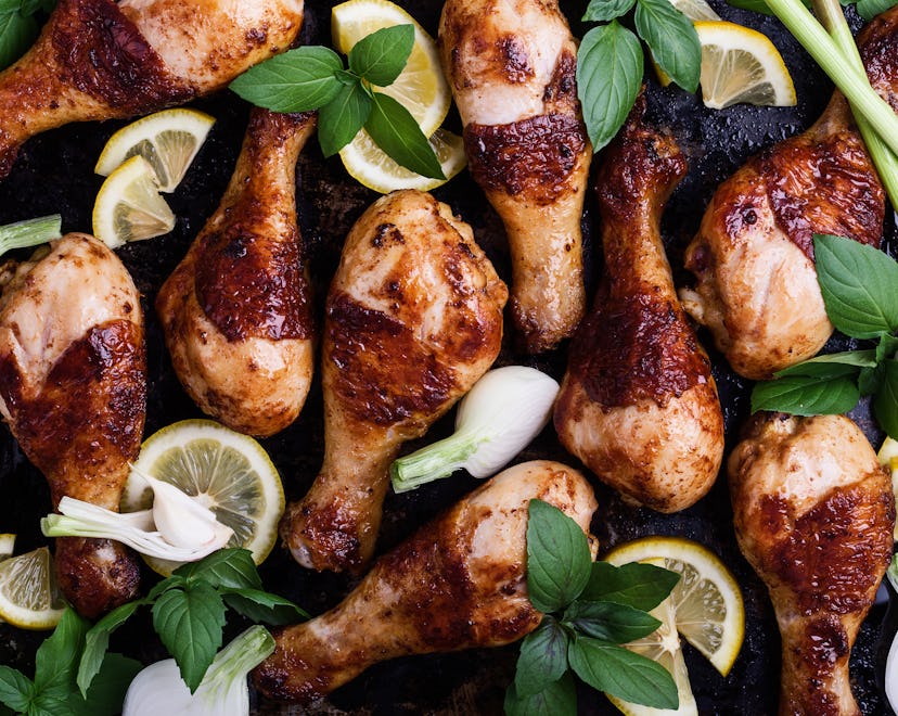 Roasted chicken legs with lemon slices. onion, garlic and basil herbs on rural baking tray viewed fr...