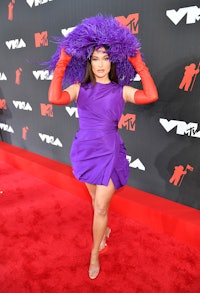 Kacey Musgraves is seen wearing a large purple, feathered headpiece on the 2021 VMAs red carpet