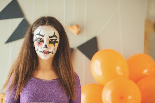Young girl is getting ready for a costume party. She has got clown face paint. Copy space shot.