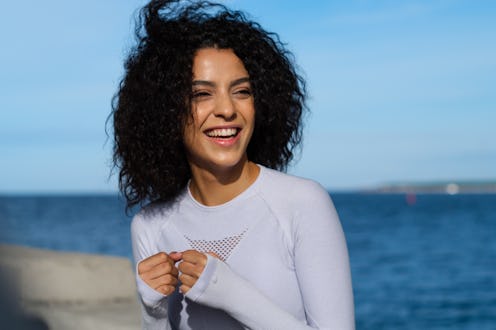 The close - up of an attractive laughing female runner in a white running suit standing against the...