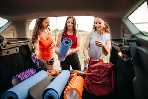 Group of young women preparing equipment in car trunk for fitness training in nature