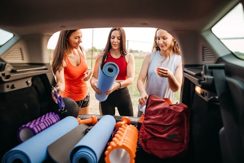 Group of young women preparing equipment in car trunk for fitness training in nature