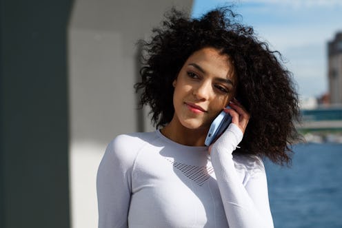 Fit attractive female  runner in a white running suit with a long sleeve is calling on the phone wit...