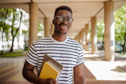 Portrait of an African-American student carrying a notebook and a laptop in front of the University