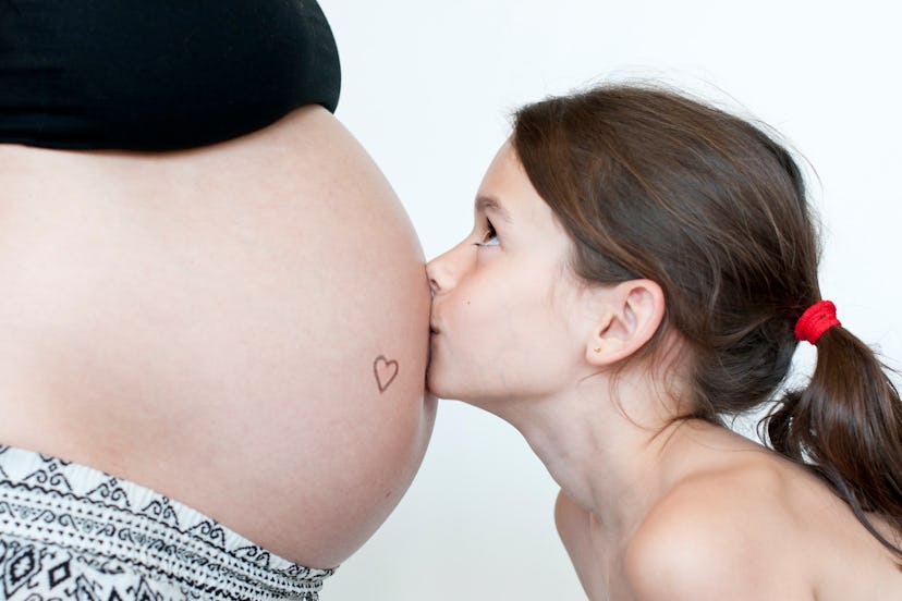Girl kissing mom's belly bump with tattoo