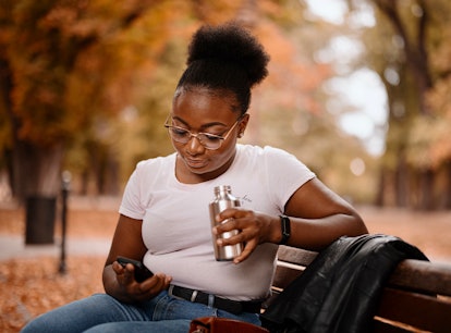 Young  black woman uses the smartphone while sitting on a park bench. Autumn concept