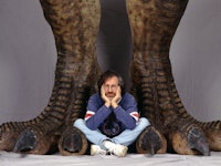 American director Steven Spielberg poses between a pair of giant dinosaur feet in a publicity still ...