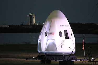 A full-size model of the Crew-1 spacecraft module sits near the launch pad as a SpaceX Falcon 9 rock...