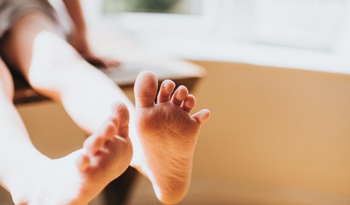 Cute little bare feet hanging off the side of a chair in sunny room. Skin wrinkled after having a ba...