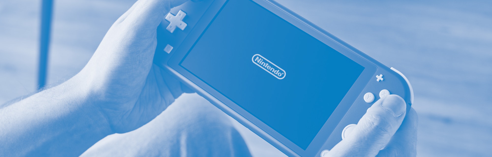 Detail of a person holding and playing a 2019 Nintendo Switch Lite handheld video games console with...