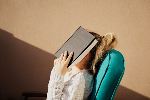 Beautiful young woman covering her face with a book in a house. Student is tired of studying or read...