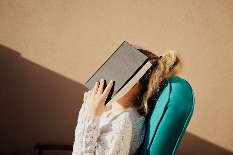 Beautiful young woman covering her face with a book in a house. Student is tired of studying or read...