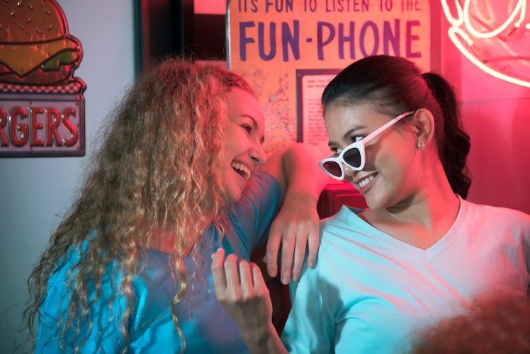 two women laughing and smiling at each other as they discuss their zodiac sign's favorite drink