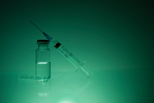 A plastic syringe is on a bottle of medicine. green blue background, cure for the virus, coronavirus...