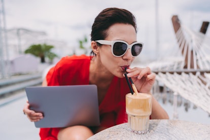 Woman at beach cafe drinking coffee frappe and using laptop