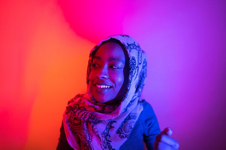 Portrait of a beautiful woman wearing a hijab, under neon lights; studio shot, isolated.
