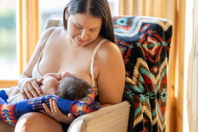 A beautiful photo of a young indigenous mother breastfeeding her newborn child. She is sitting on a ...