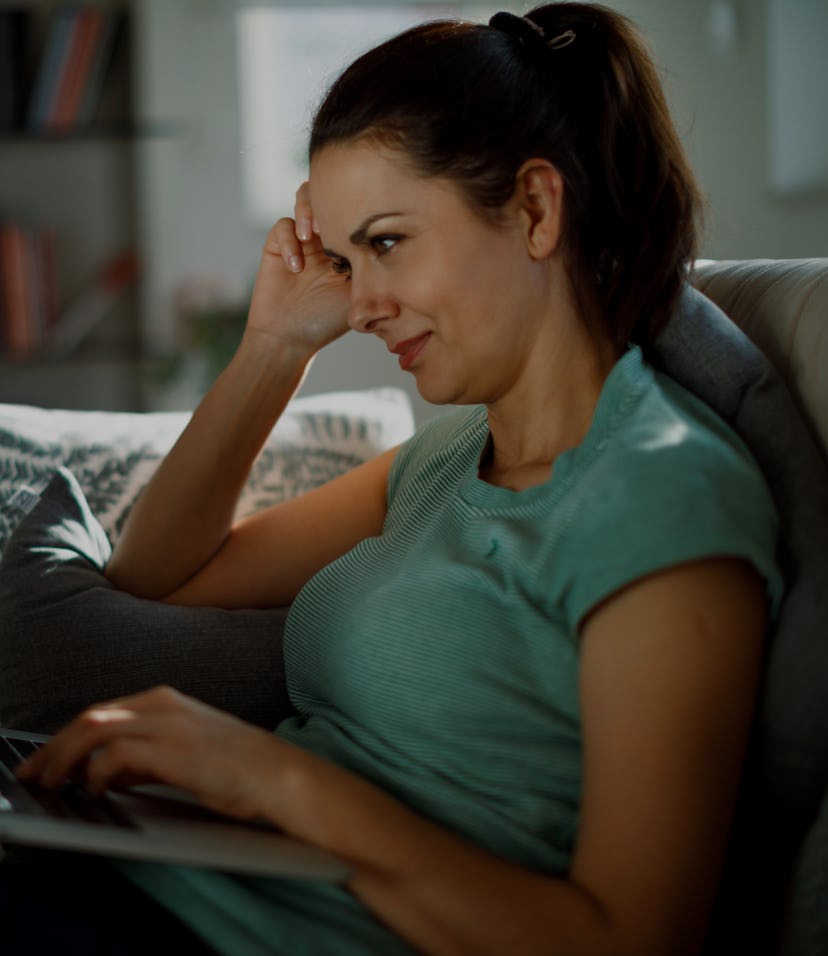 Smiling relaxed woman resting on couch using laptop