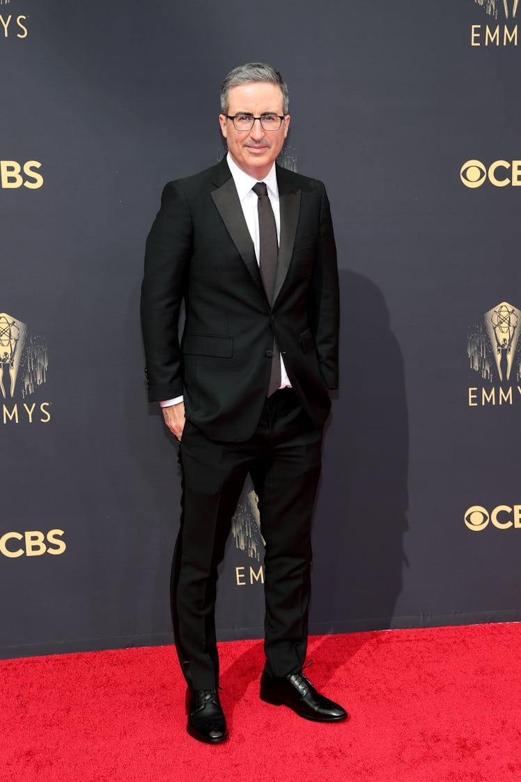 John Oliver in a black suit, a white shirt, and a black tie at the Emmys Red Carpet 2021