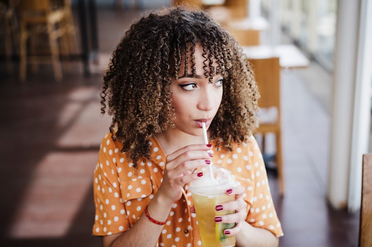 A woman drinking a hard kombucha drink at a restaurant  thinks of Instagram captions for her drink. 