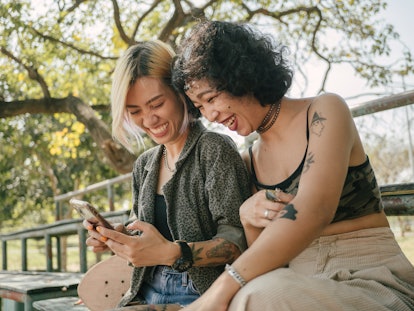 young women smiling and laughing at phone as they chat about gemini libra friendship compatibility