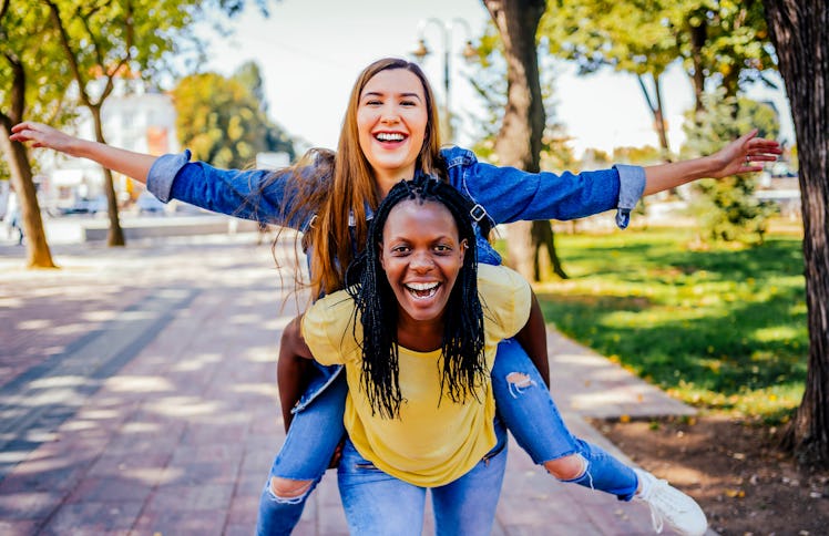two young women smiling as one gives the other a piggyback ride, while chatting about gemini libra f...