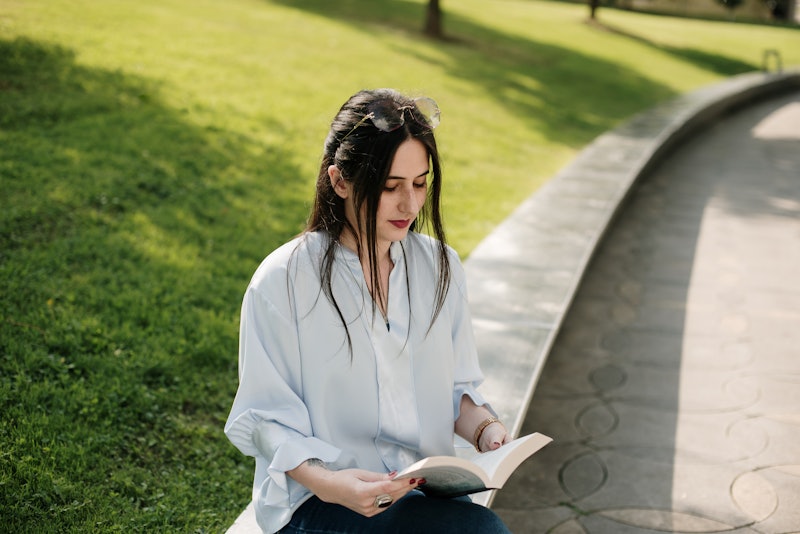 A young woman sitting in a city park and reading a book