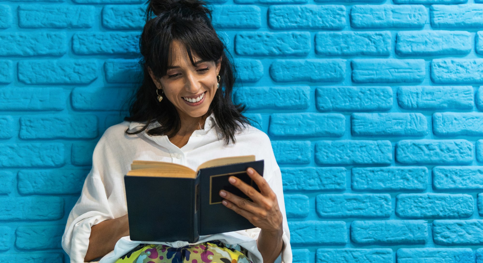 A reader in a crisp white shirt smiles at an open book.