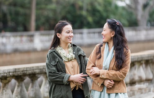 A Filipino mother and her multiracial teenage daughter standing arm in arm at a public park, smiling...