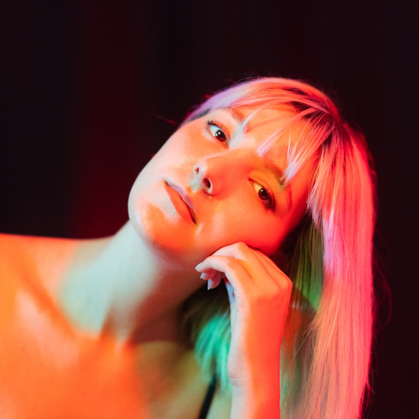 Young woman sitting in colorful neon light ahead of Mercury retrograde in Libra fall 2021, which has...