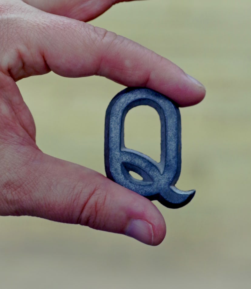 Caucasian male hand holding a metal letter q in his fingers