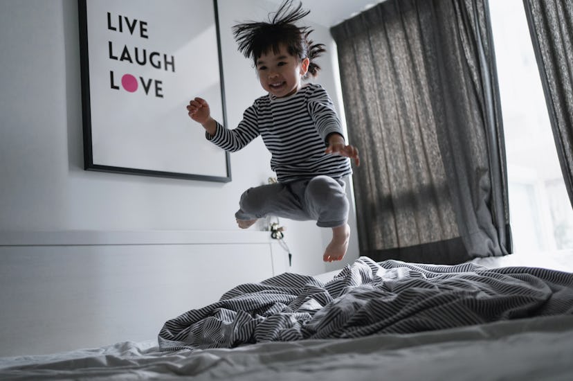 Playful little Asian girl jumping on the bed at home, having fun in bed. Simple happiness