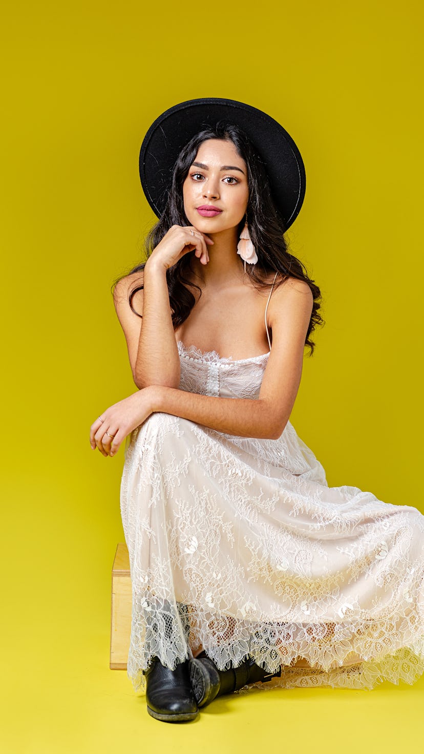 A portrait of attractive young woman wearing bohemian style dress and a black fedora hat, sitting in...