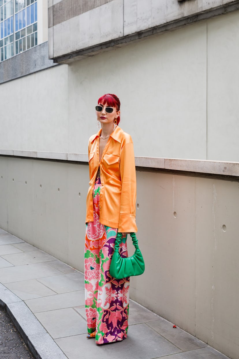 LONDON, ENGLAND - SEPTEMBER 19: A guest wearing an orange shirt, flower print trousers and a green b...