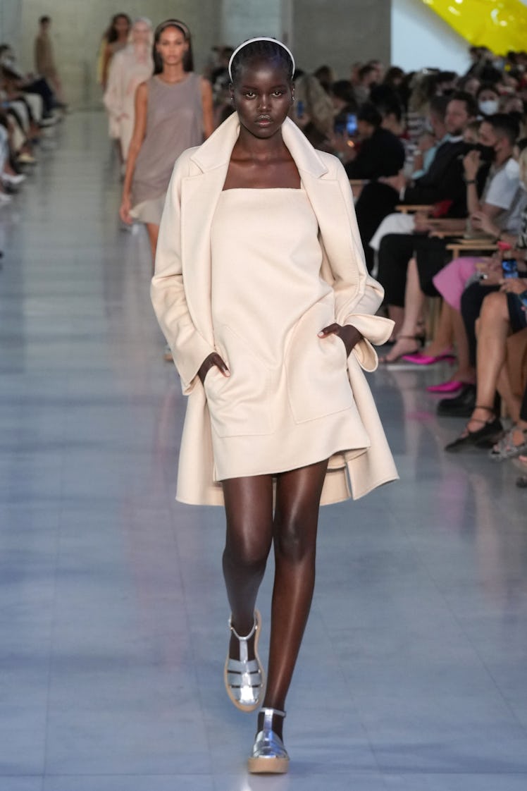 Adut Akech walking the Max Mara fashion show at Milan Fashion Week Spring 2022 in a cream-colored dr...