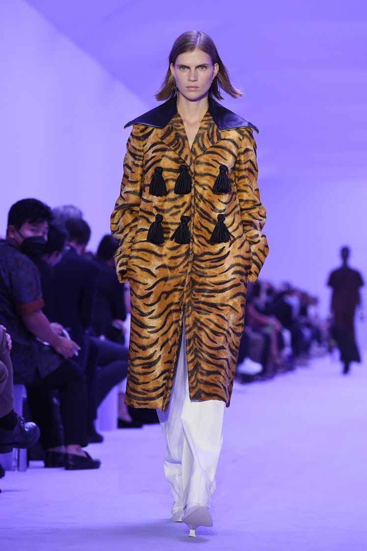 A model walking the Jil Sander show at Milan Fashion Week Spring 2022 in a tiger-print coat and whit...