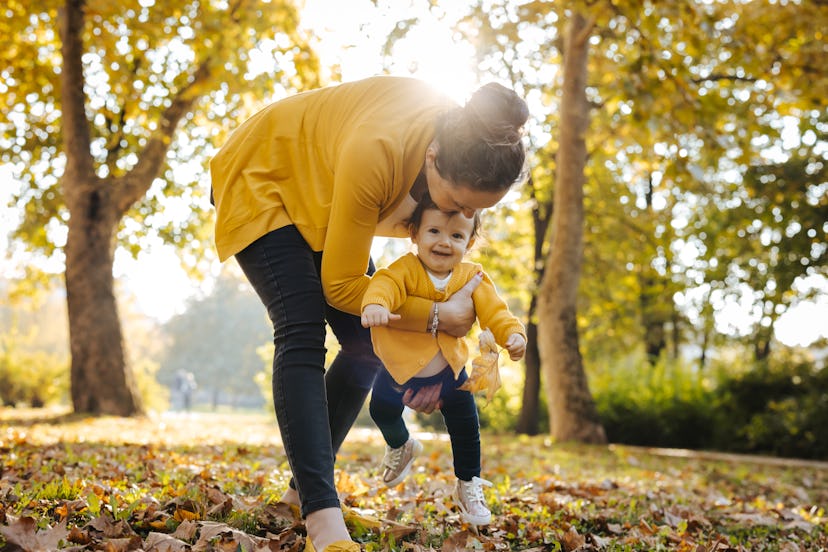 Mother is teaching her daughter to walk in sunny autumn park