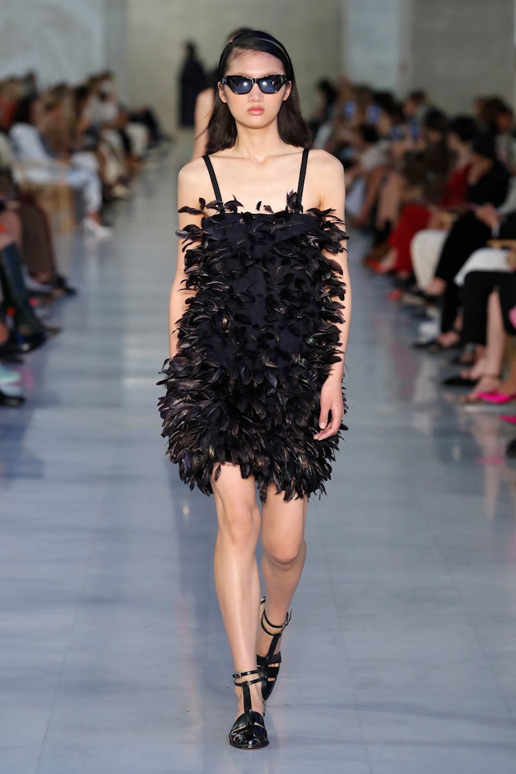 A model walking the Max Mara fashion show at Milan Fashion Week Spring 2022 in a feathered black dre...