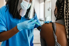 Rear view of an African American adult woman receiving the COVID-19 vaccine by nurse o female doctor...