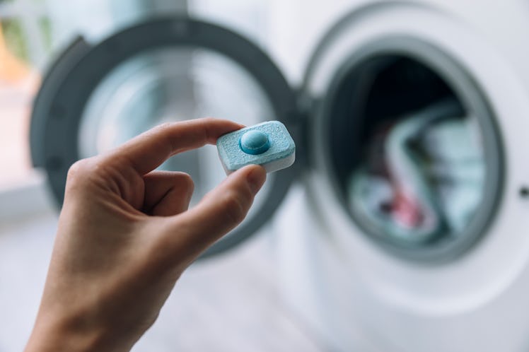 Close up of hand holding detergent capsule in front of washing machine