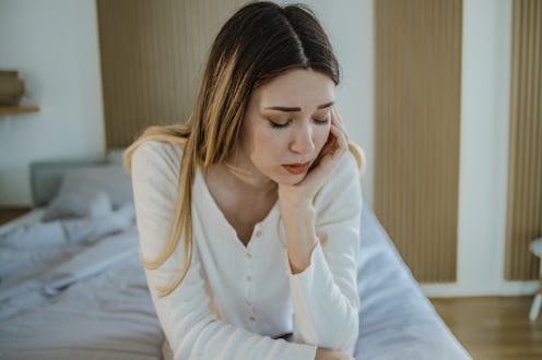 A sad young woman in bed suffers from depression and she is having a headache