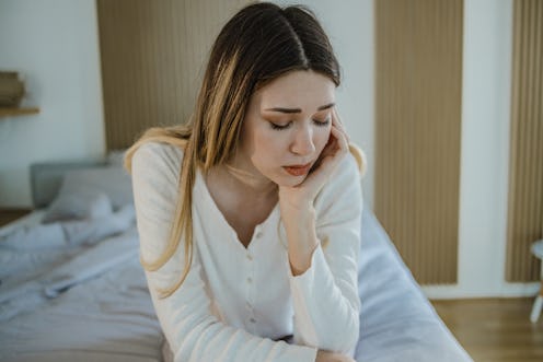 A sad young woman in bed suffers from depression and she is having a headache