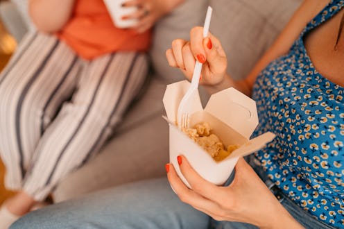 Woman eating her ordered lunch at home with friend. Eating pasta. Close up.