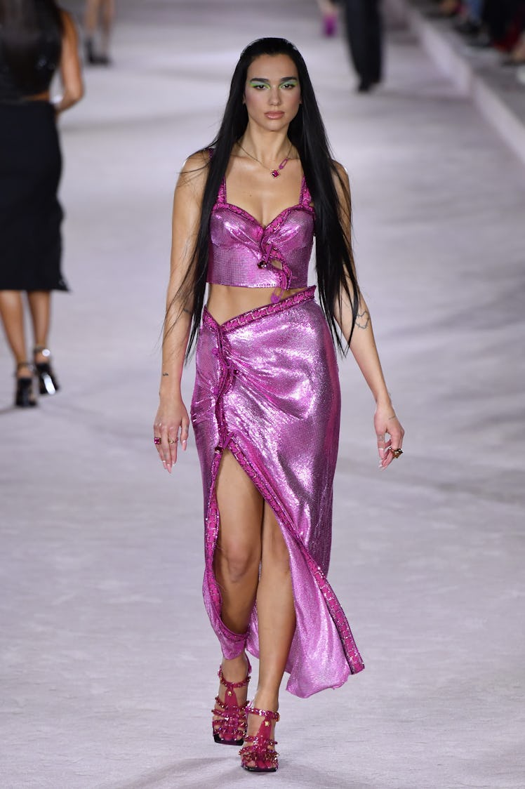 Dua Lipa on the runway of Versace Ready to Wear Spring/Summer 2022 in a shimmery purple top and skir...