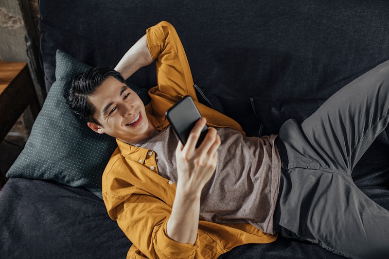 A happy student lying on the couch and video chatting with his friends.