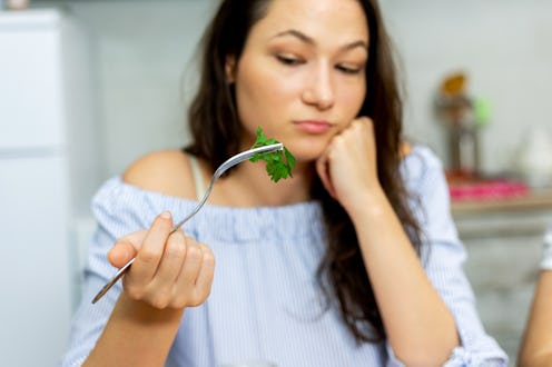 Shot of a young woman eating a healthy salad at home.She dosen't like to eating green