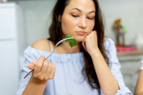 Shot of a young woman eating a healthy salad at home.She dosen't like to eating green