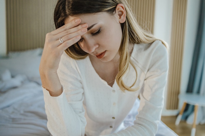 A sad young woman in bed suffers from depression and she is having a headache