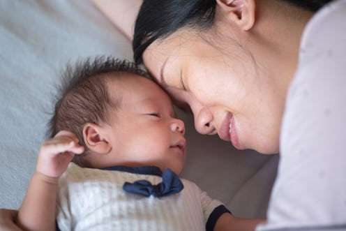 Mother and newborn baby boy having a cute moment while baby lying on the bed. Asian woman with 400 d...